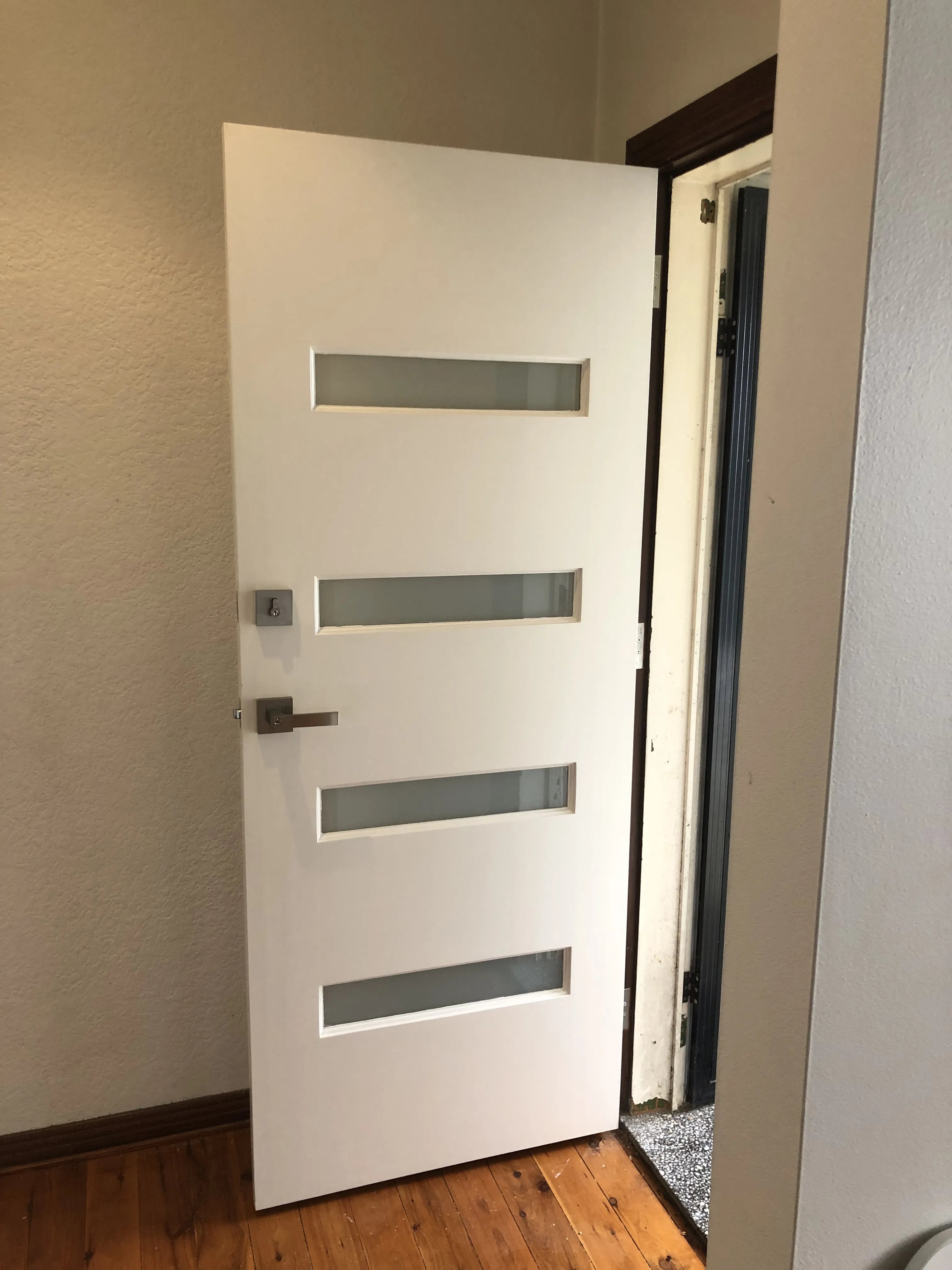 Modern front door with 4 horizontal frosted glass panels. Door is painted white and has chrome combination lock installed.