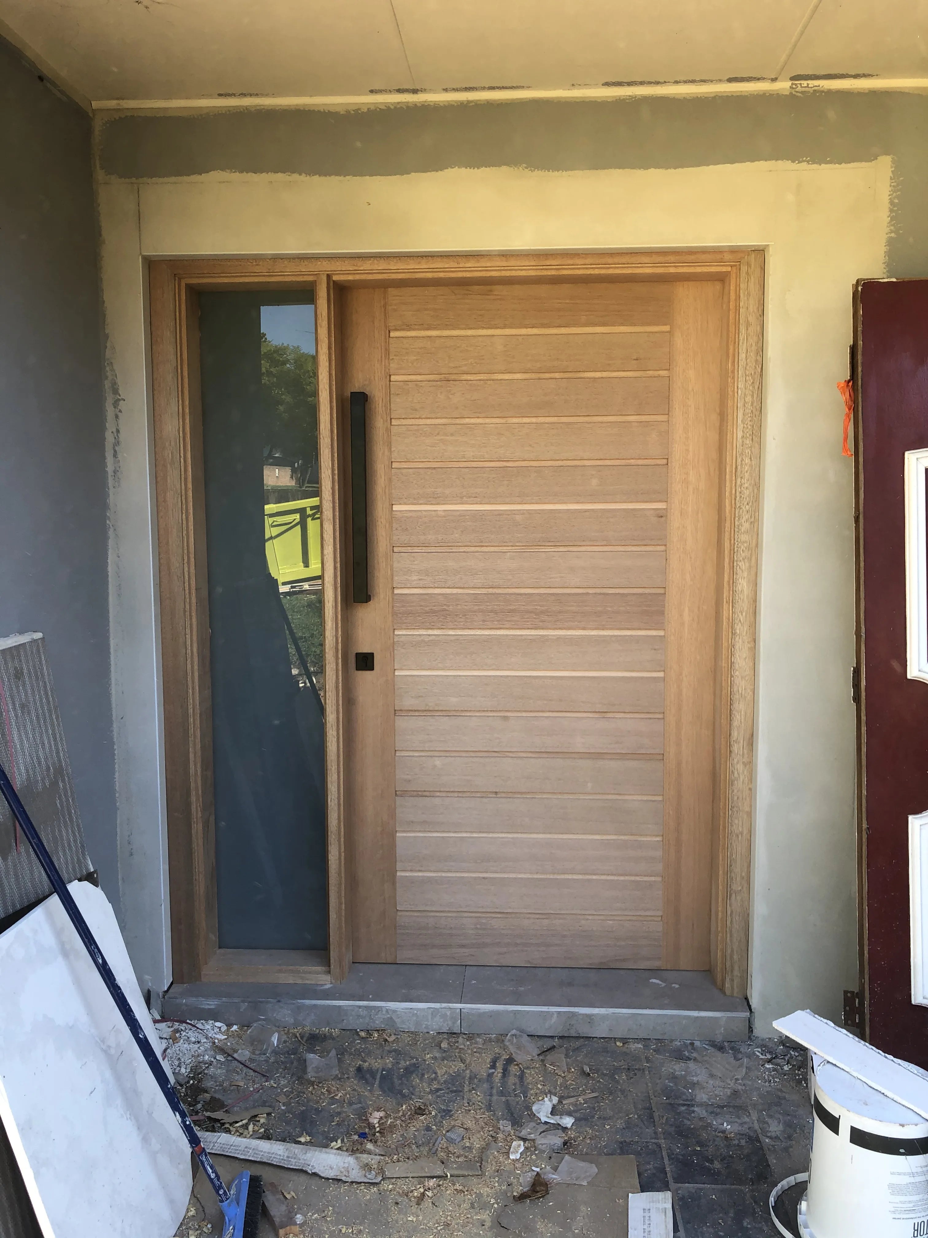 Modern wood 1200mm door installed with one fixed side panel of frosted glass. 600mm Black pull handle and mortice lock installed on door.