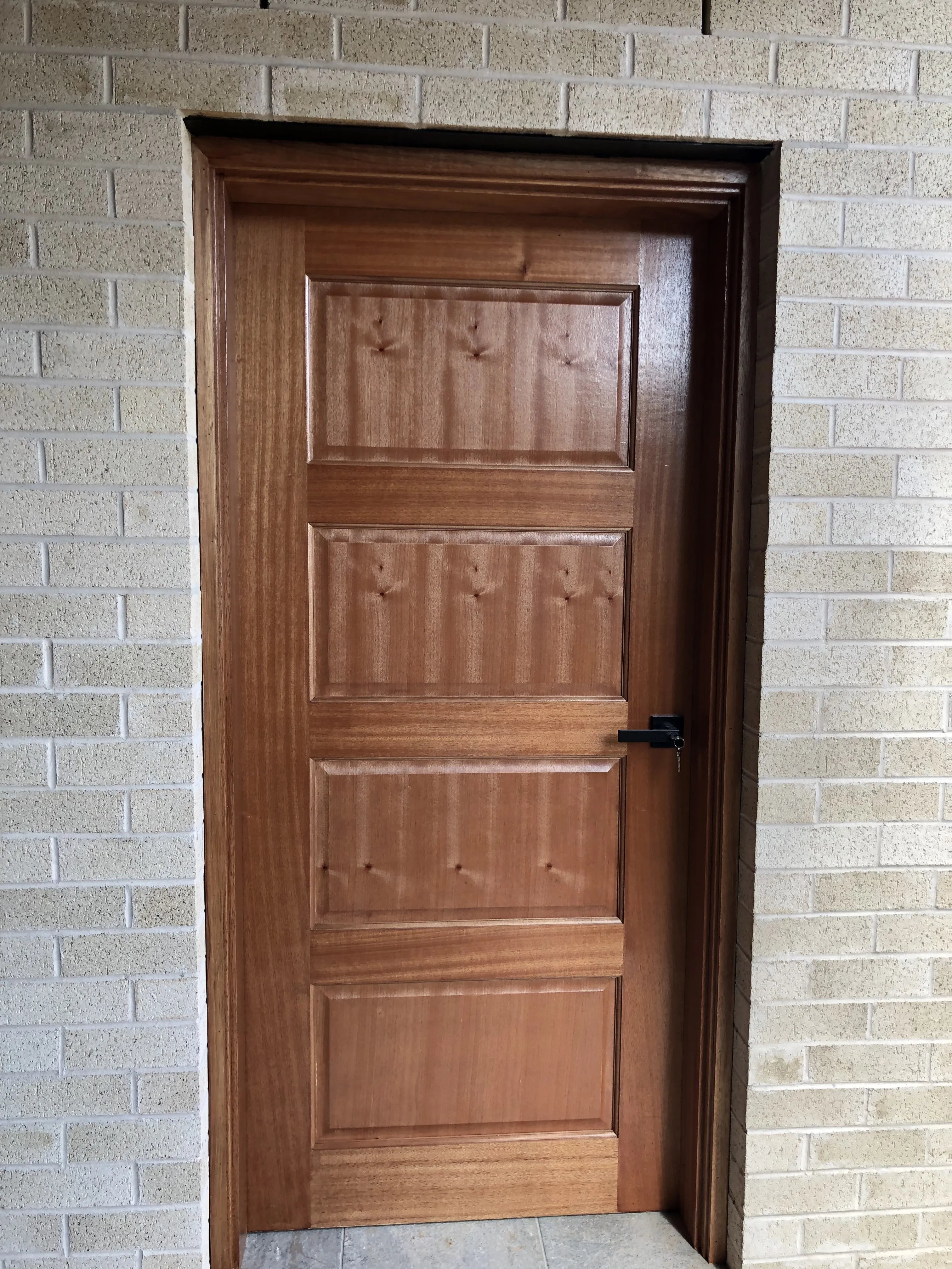 Classic style 4 panel external door. Black entrance handle installed on door that is stained and varnished.